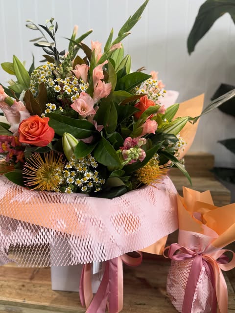 A peach and coral bouquet of roses, lisianthus and daisies wrapped in pink paper