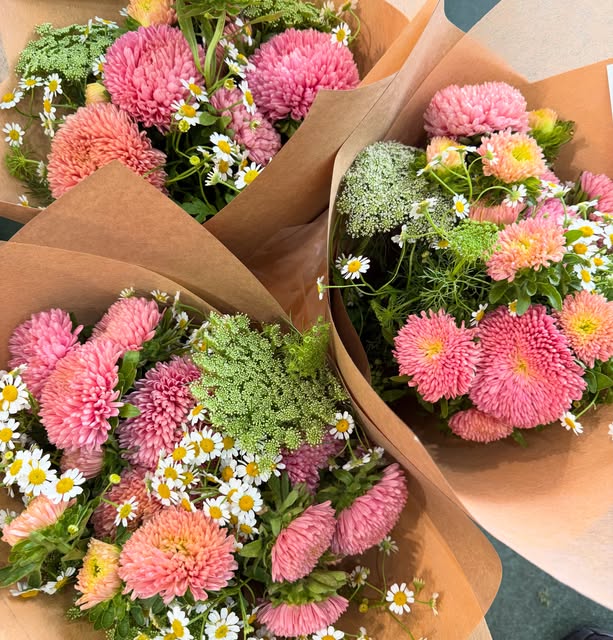 Three pink and coral market bunches wrapped in brown paper